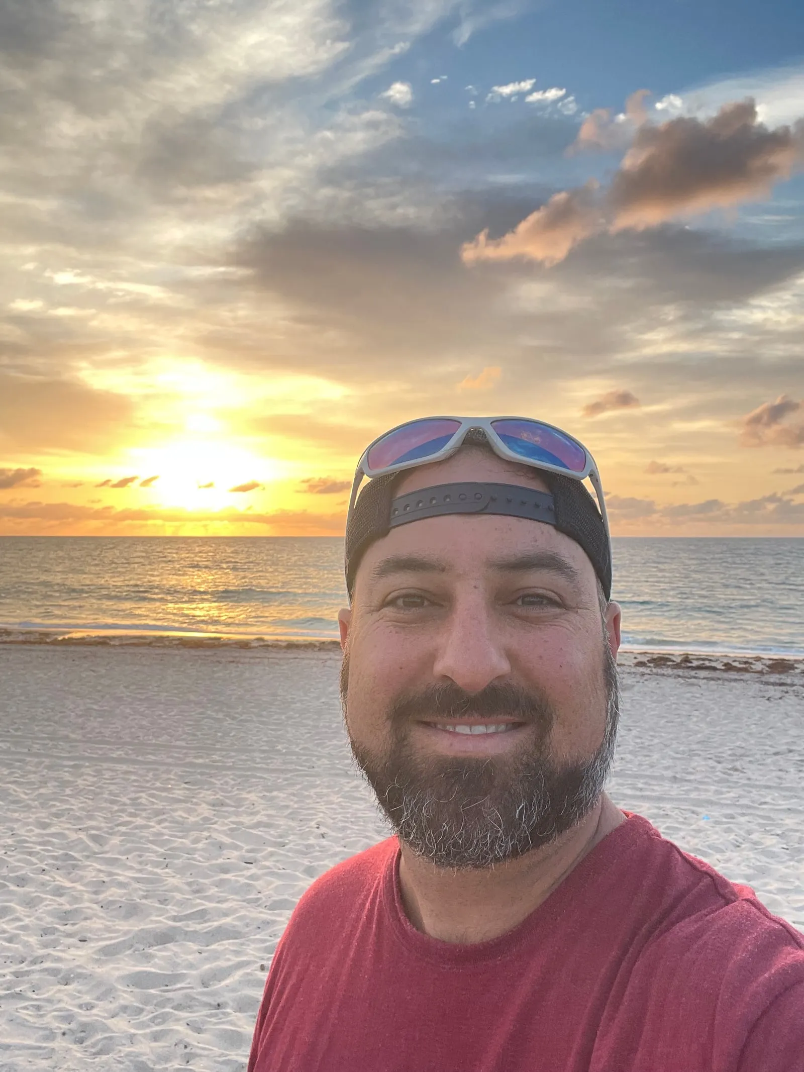 Hakim smiling on the beach, with the sun low over the ocean behind him
