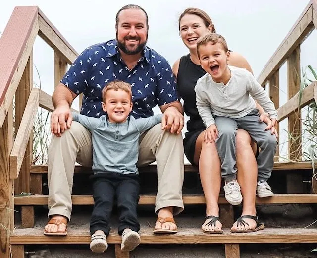 Hakim with his wife and their identical twin boys on beach steps