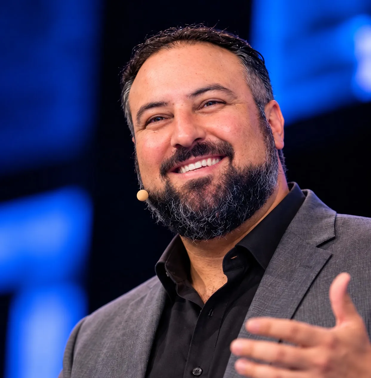 Hakim smiling as he speaks on stage, wearing a headset microphone